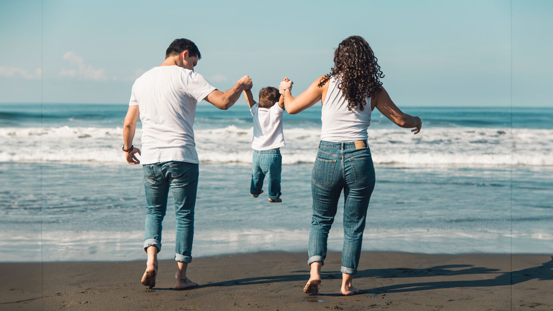 Mom, dad, and young child laughing and playing together on a sandy beach in Marathon, Florida, enjoying their family vacation.